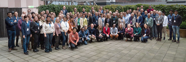 Photo showing a  big group of people standing and sitting outside 