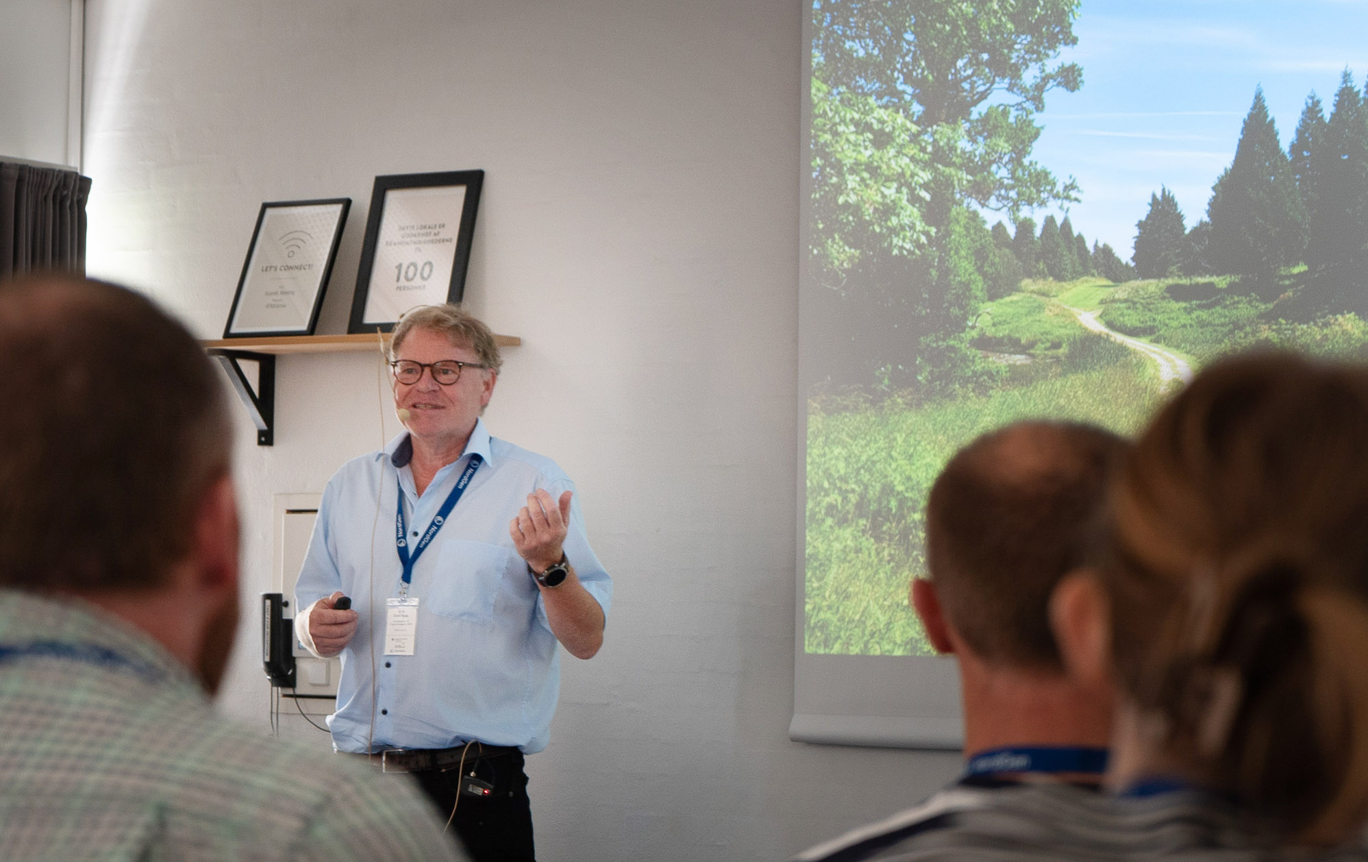 A person talking during a presentation, a photo of forest is projected in the background.