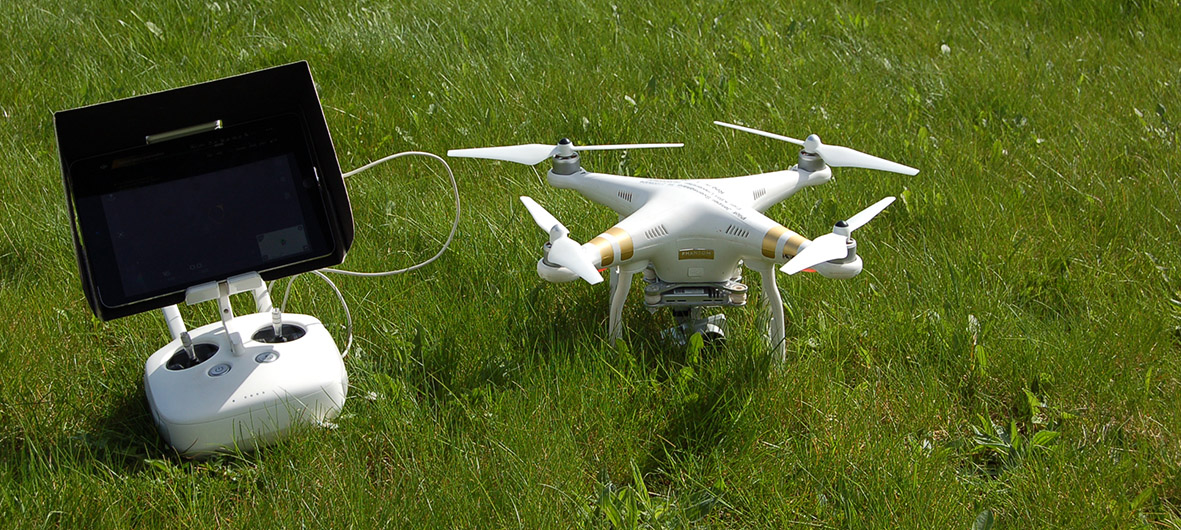 A drone and its remote control, placed on a lawn.