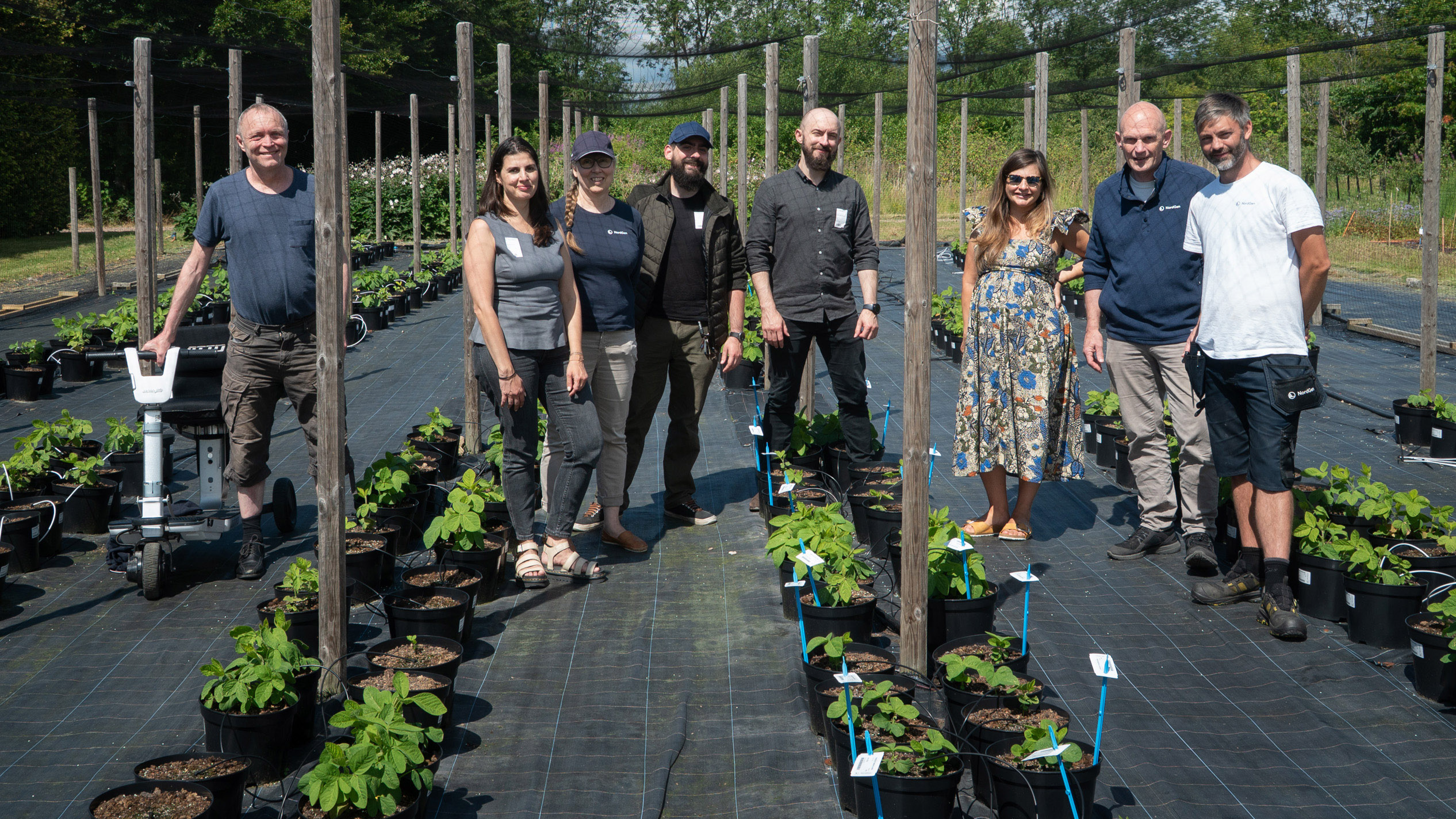 Group of people standing outside in front of rows of plants in pots
